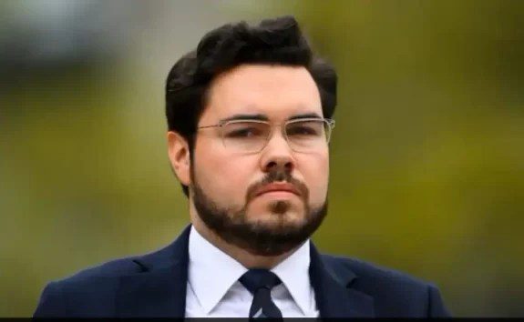 Man with glasses wearing a suit outdoors.