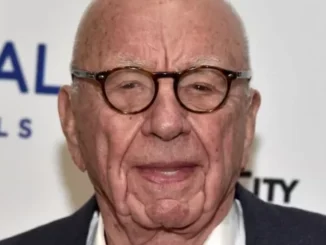 Elderly man with glasses, smiling at event.