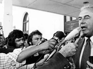 Politician speaking to reporters with microphones.