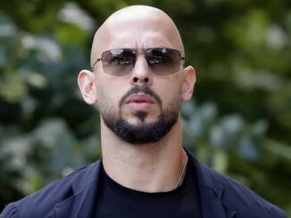 Bald man wearing sunglasses outdoors, blurred background.