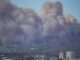 Large smoke clouds over city skyline.