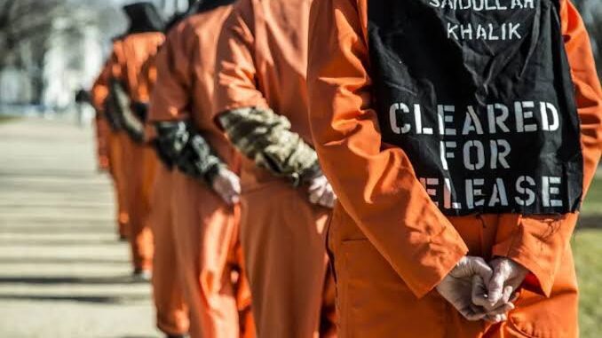 People in orange jumpsuits standing in line.