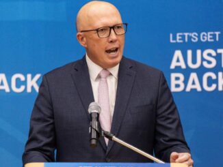 Man speaking at podium with blue background.
