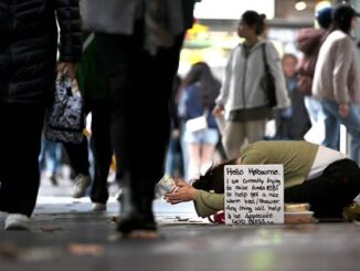 Person kneeling with sign on busy street.