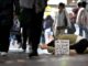 Person kneeling with sign on busy street.