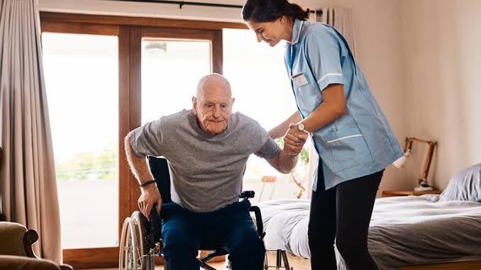 Caregiver assisting elderly man from wheelchair.