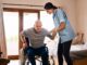 Caregiver assisting elderly man from wheelchair.