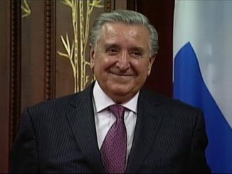 Smiling man in suit with flag background.