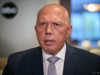 Man in suit speaking indoors, blurred background.