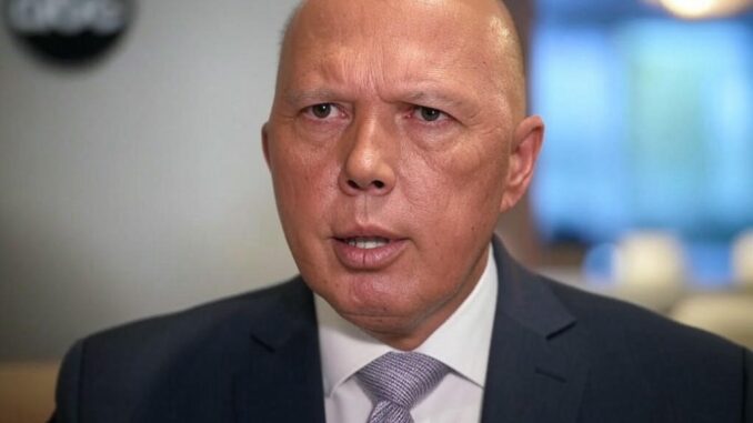 Man in suit speaking indoors, blurred background.