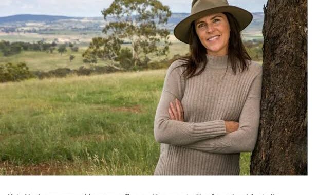 Woman in a hat standing by tree.