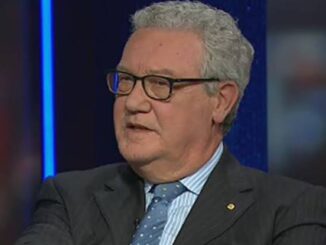 Man in suit speaking on television set.