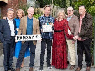 Group of people standing with Ramsay Street sign.