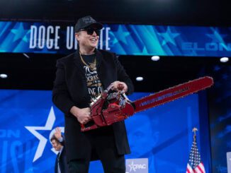 Person holding chainsaw on stage, smiling.