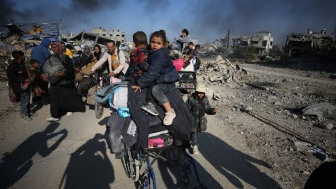 People amidst rubble and destruction, carrying belongings.