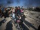 People amidst rubble and destruction, carrying belongings.
