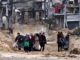 People walking through a war-torn street.