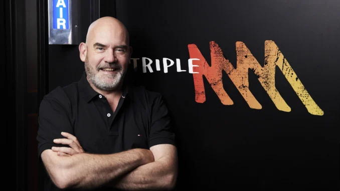 Man standing next to Triple M logo. Man standing next to Triple M logo.