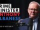 Man speaking into a microphone, text overlay.