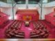 Empty parliamentary chamber with red seating arrangement.