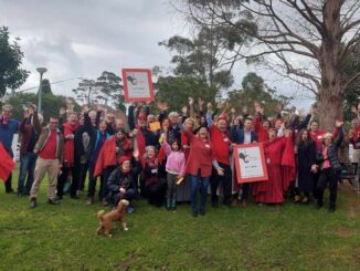 Group celebrating outdoors with signs and dog.