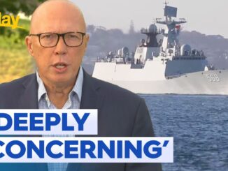 Man speaking with warship in background.