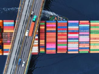 Bridge over colorful shipping containers on water.