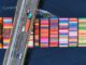 Bridge over colorful shipping containers on water.