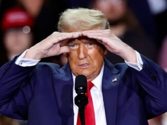 Man shielding eyes while speaking at event.