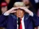 Man shielding eyes while speaking at event.