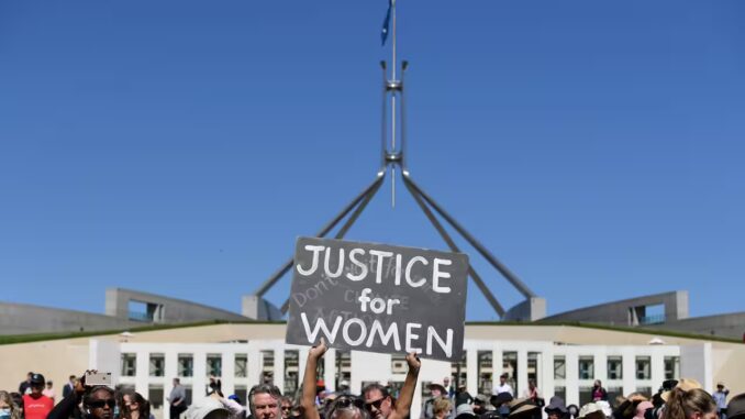 Protesters holding "Justice for Women" sign outside building.