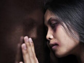 Woman with tear-streaked face against wall.