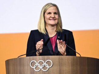 Woman speaking at Olympic-themed podium.