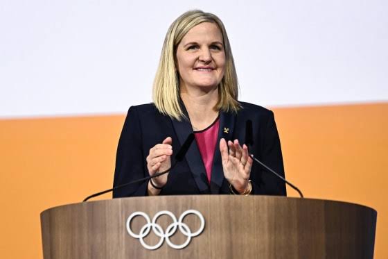 Woman speaking at Olympic-themed podium.