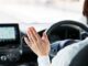 Person gesturing inside car, dashboard visible.