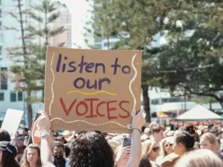Protest crowd with "listen to our voices" sign.