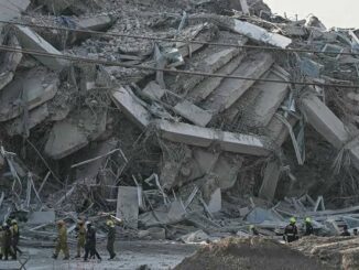 Collapsed building with rescue workers present.