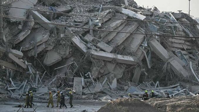 Collapsed building with rescue workers present.