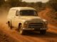 Vintage van driving on a dusty road.