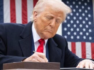 Person signing document in front of flag.