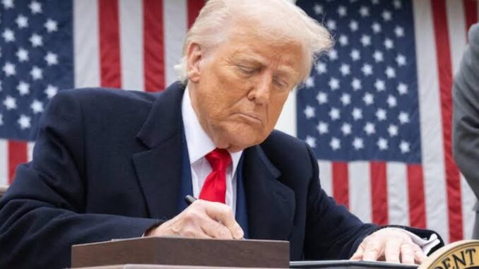 Person signing document in front of flag.