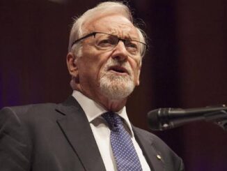 Bearded speaker wearing glasses and patterned tie