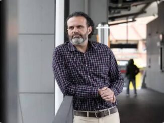 Man leaning on railing, urban background.