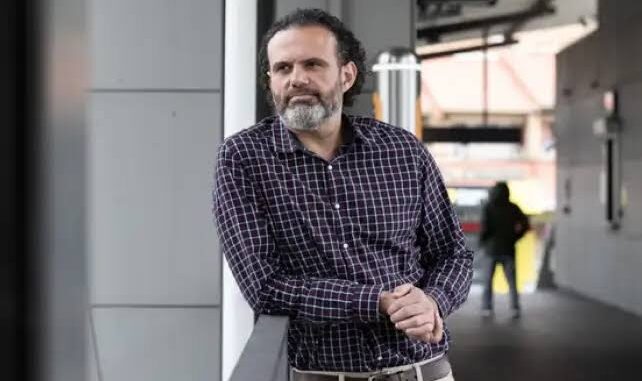 Man leaning on railing, urban background.
