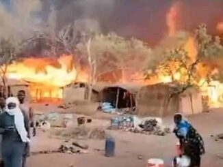 Huts on fire with people nearby.