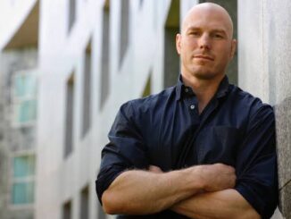 Bald man in black shirt, leaning outdoors.
