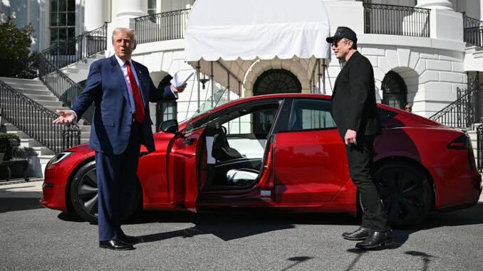 Two men standing by a red car.