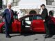 Two men standing by a red car.
