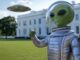 A toy alien figure poses in front of the White House on a sunny day.