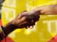 Two people shaking hands in front of a yellow background.